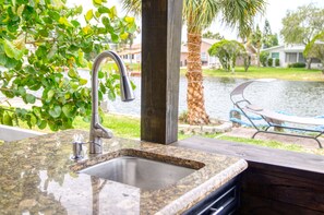 A kitchen with a granite countertop, stainless steel sink, and a view of a backyard with a pool and palm trees. - A wonderful space to relax and unwind. Perfect for family or intimate occasion. (NEW PRT RCHY)