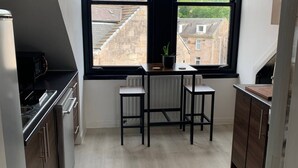 Een moderne keuken met een eethoek, grote ramen en uitzicht op gebouwen.
