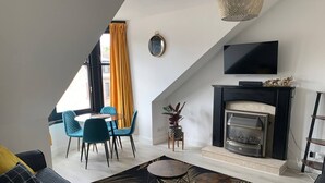 Een moderne woonkamer met een open haard, een flatscreen televisie en een eethoek met stoelen en een tafel.