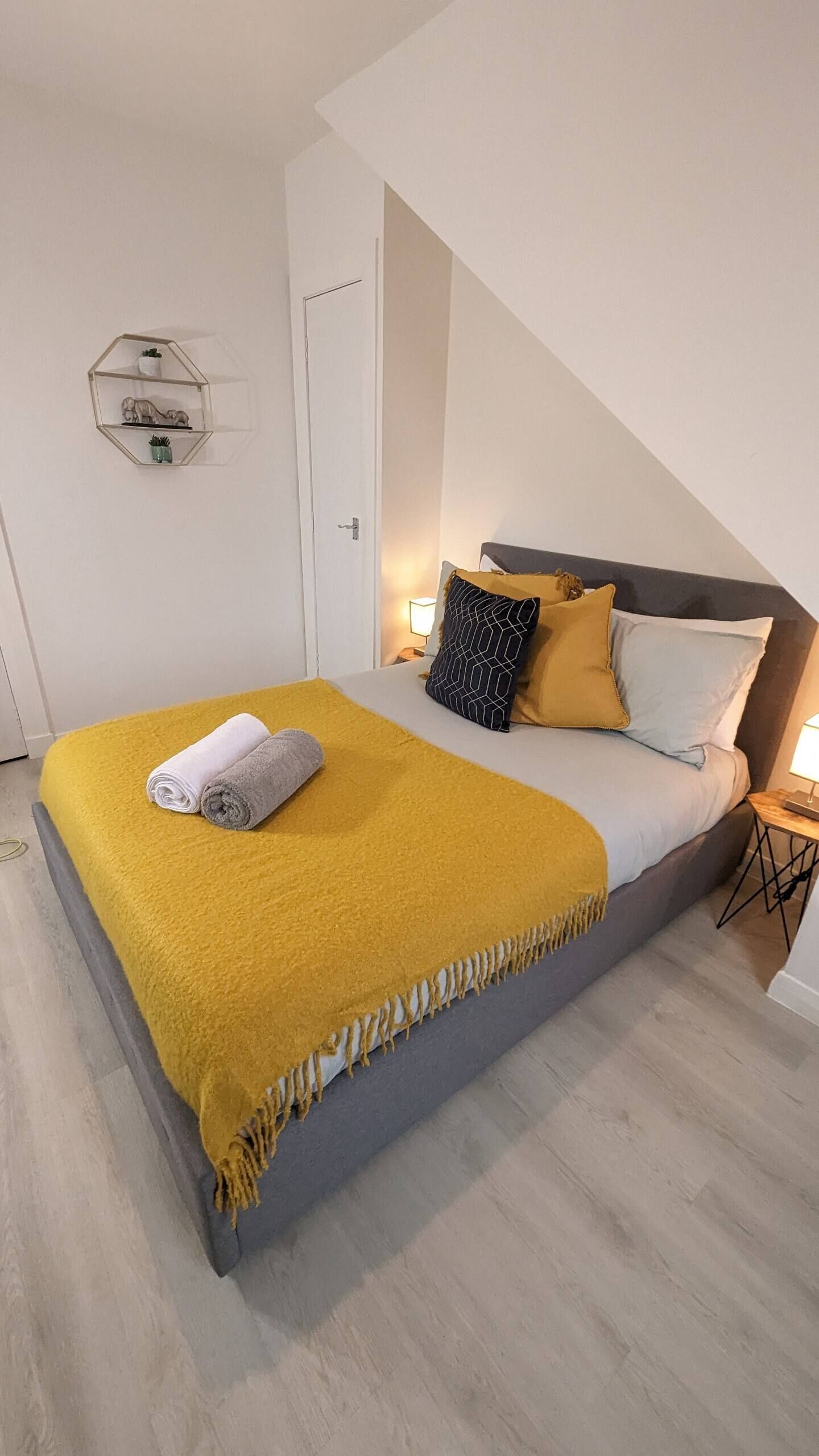 A modern bedroom with a bed, a yellow throw blanket, and a geometric wall shelf.