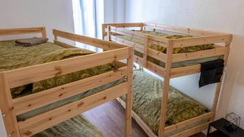 A room with three bunk beds, each with a green patterned mattress, a wooden frame, and a small table with a lamp beside it.