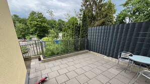 Un espace patio doté d’un sol carrelé, d’une clôture en métal, d’une table avec des chaises et d’un jouet rouge.