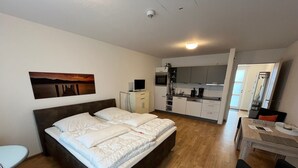 Une chambre avec un grand lit, un bureau et, au fond, un coin cuisine.