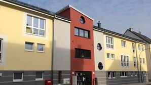 Un immeuble à plusieurs étages, avec une façade jaune, une partie rouge et une partie inférieure grise.