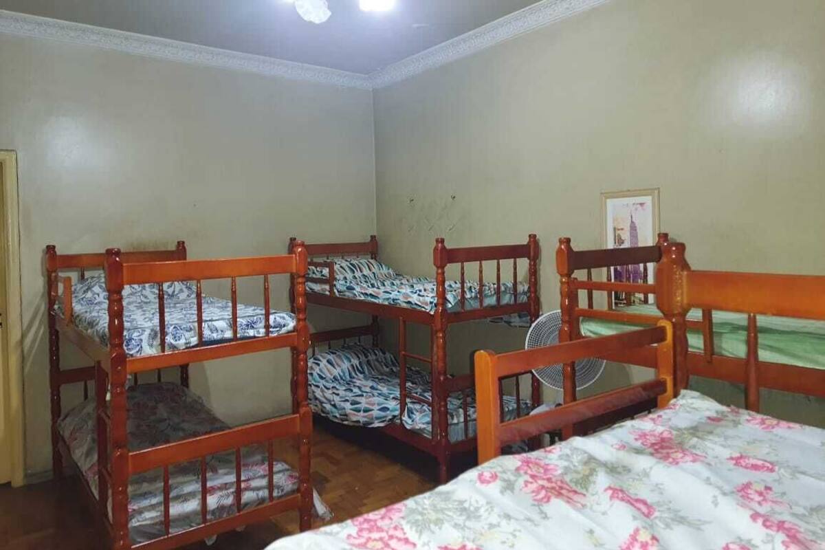 A room with four wooden bunk beds, a ceiling fan, and a framed picture on the wall.