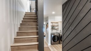 Un escalier menant à une buanderie, avec un revêtement de sol en bois et une porte noire.