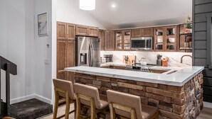 Une cuisine moderne dotée d’un îlot central, de meubles en bois, d’appareils électroménagers en acier inoxydable et de luminaires suspendus.