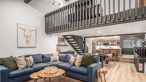 Un salon moderne avec un canapé bleu, une table basse en bois et un tapis à motifs. Un escalier mène à un niveau supérieur, lequel est doté d’une rambarde.