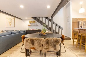 Cozy living space with a round dining table and comfortable seating. The room features a sofa, side table, and a staircase leading to an upper level.