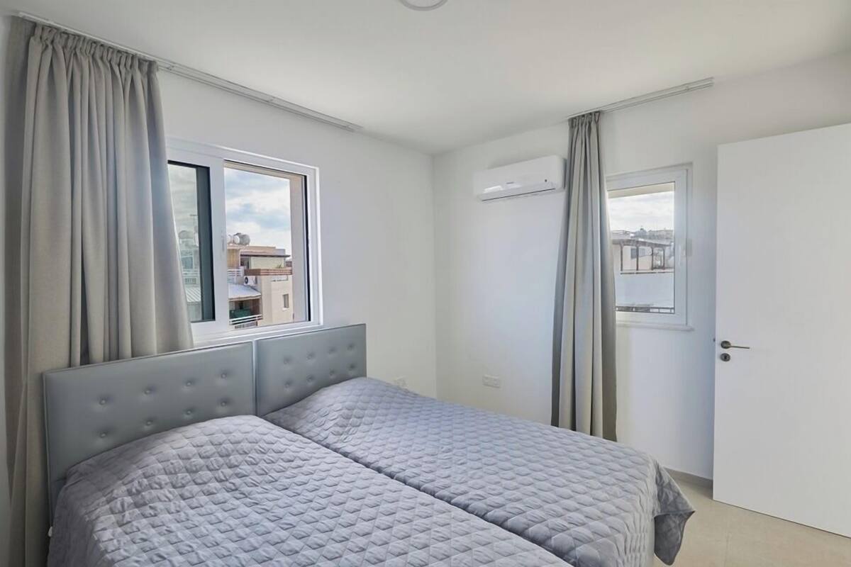 A bedroom with a bed, curtains, an air conditioning unit, and a window with a view.