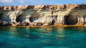 A coastal cliff with a cave entrance and clear turquoise water.