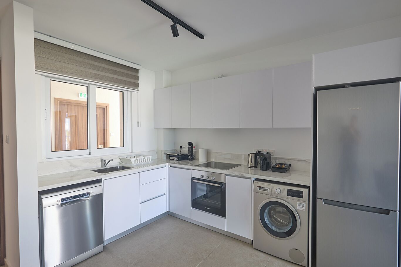 A modern kitchen with white cabinets, stainless steel appliances, a dishwasher, an oven, a washing machine, and a refrigerator.