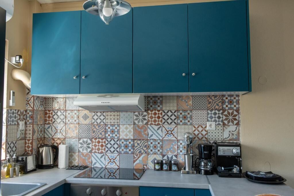 A kitchen with teal cabinets, patterned backsplash, and modern appliances including a coffee maker and toaster.