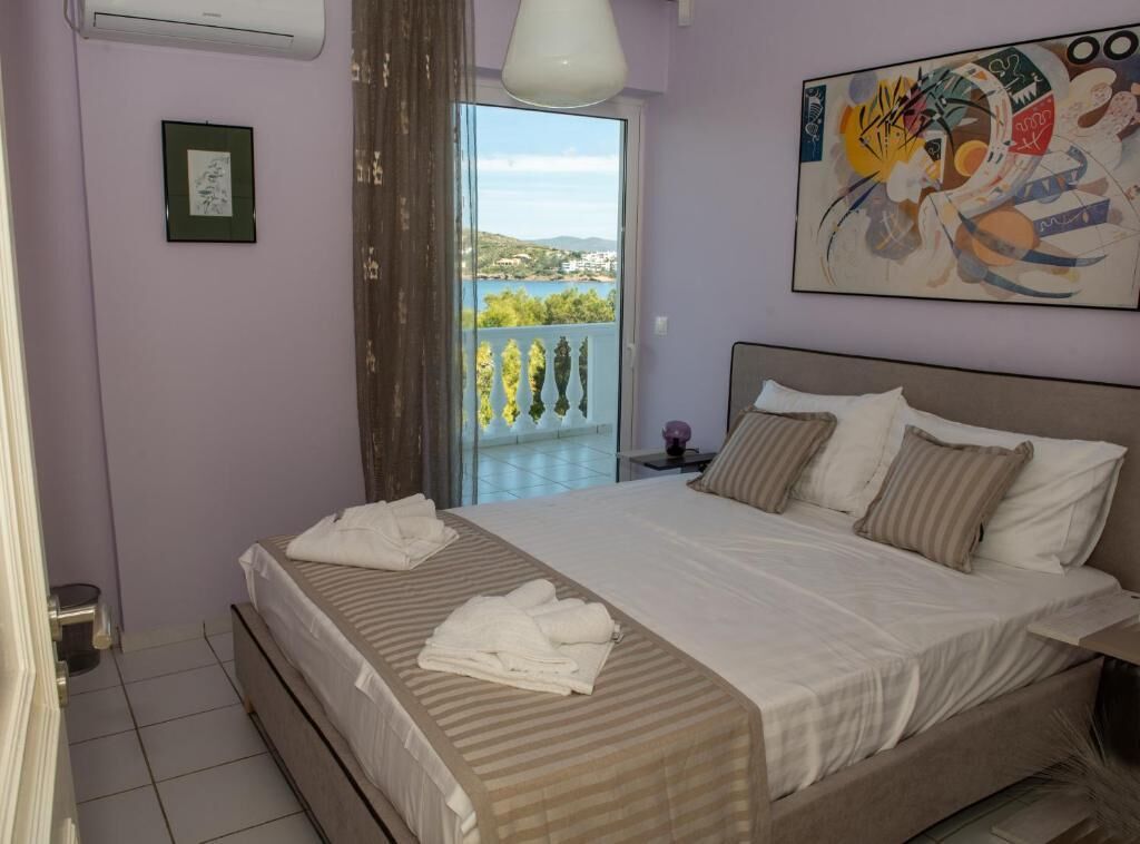 A bedroom with a bed, a bedside table, a window with a view, and a painting on the wall.