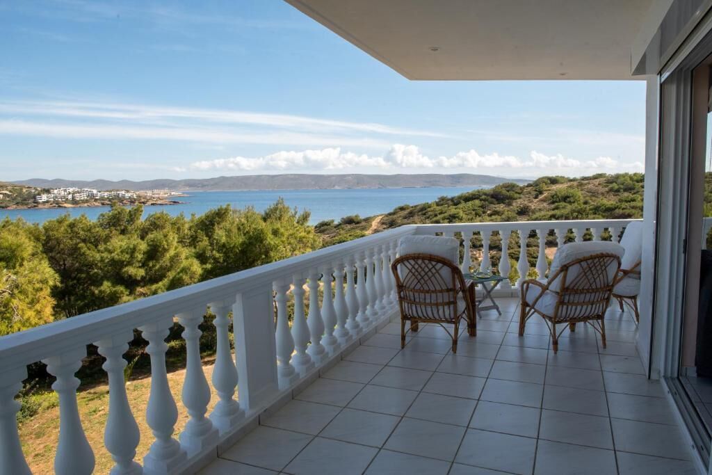 Un balcon agrémenté de deux fauteuils en osier et d’une table, offrant une vue imprenable sur le paysage côtier, la mer et les collines lointaines.