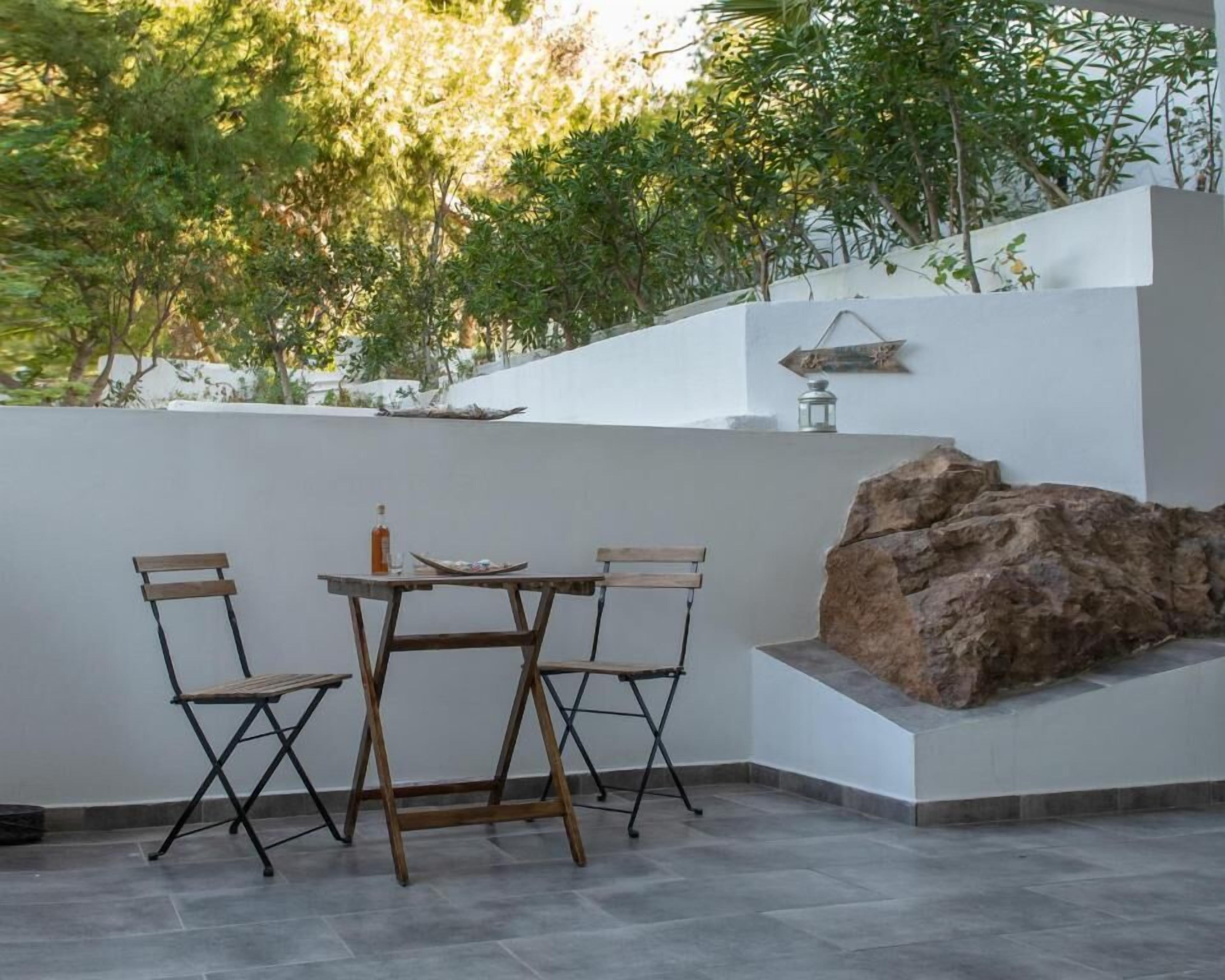 Een terras met een tafel, stoelen, een rotspartij en een lantaarn aan een witte muur.