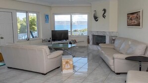 A spacious living room with a fireplace, a television, and a view of the sea. - Sounio Golden View Villas (Lavreotiki)