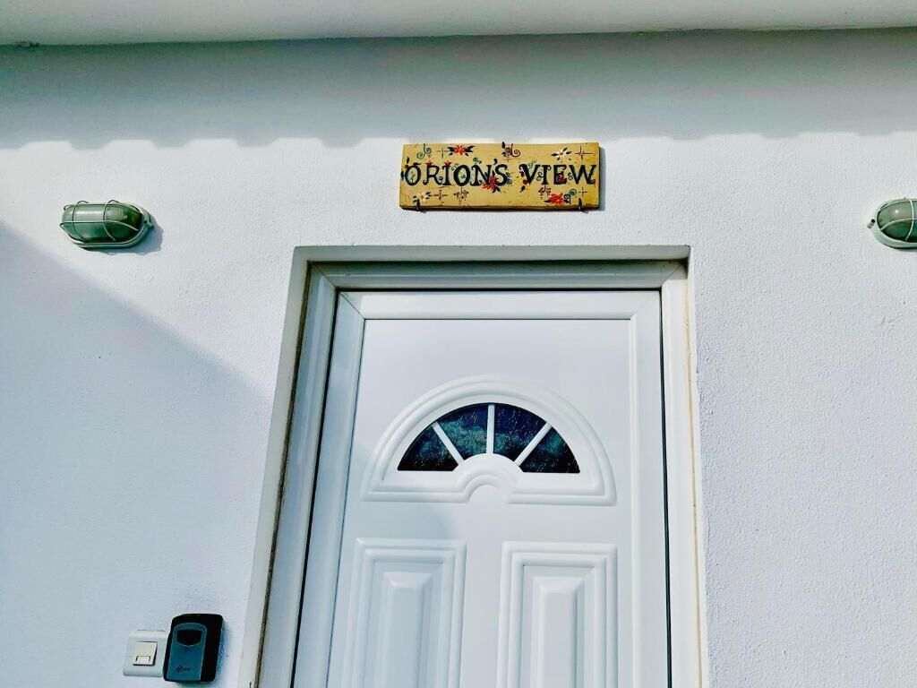 A white door with a semi-circular window and a sign above it that reads "Orion's View".