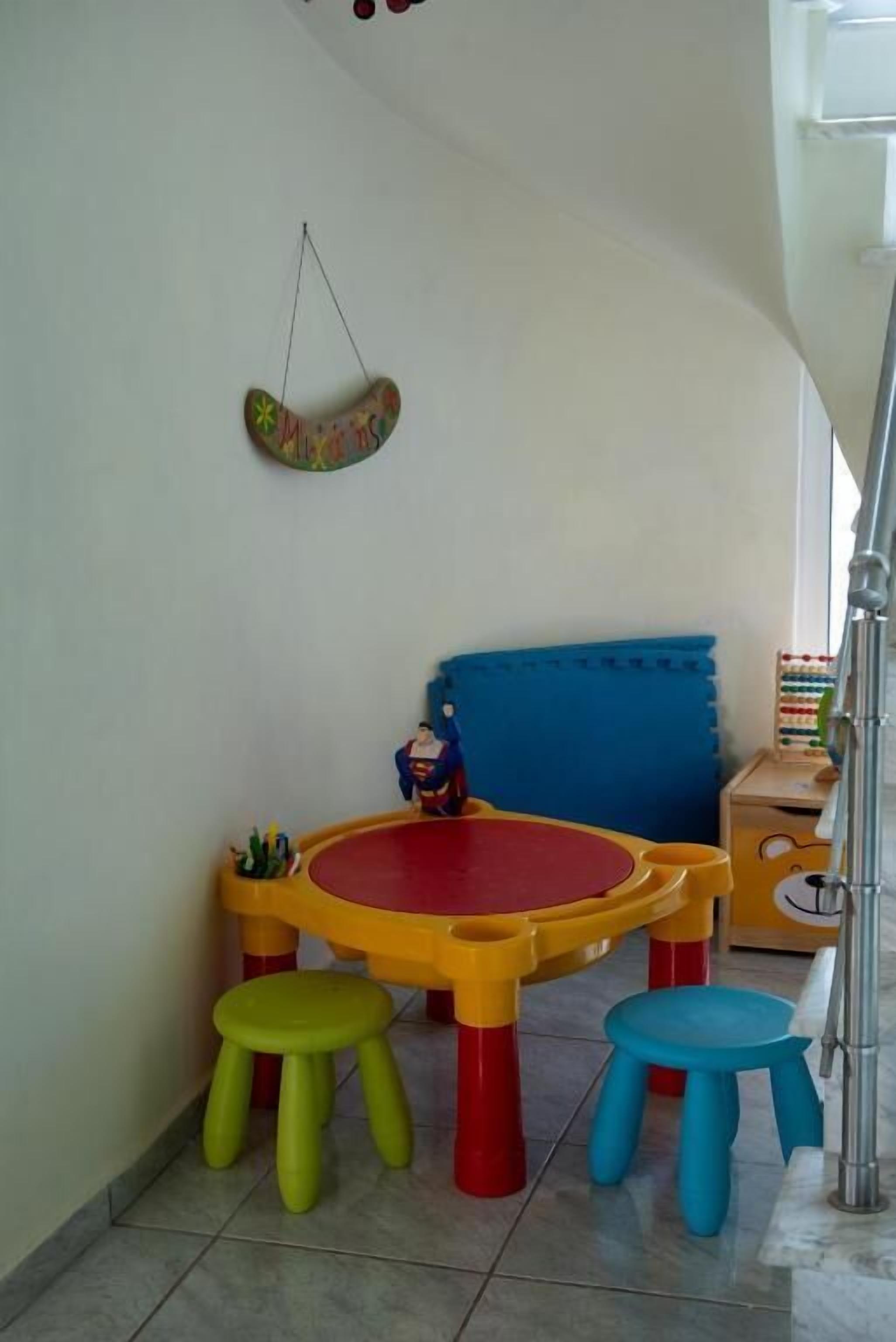 Uma área de recreação infantil com uma mesa e banquetas coloridas, um banco acolchoado azul e uma decoração pendente.