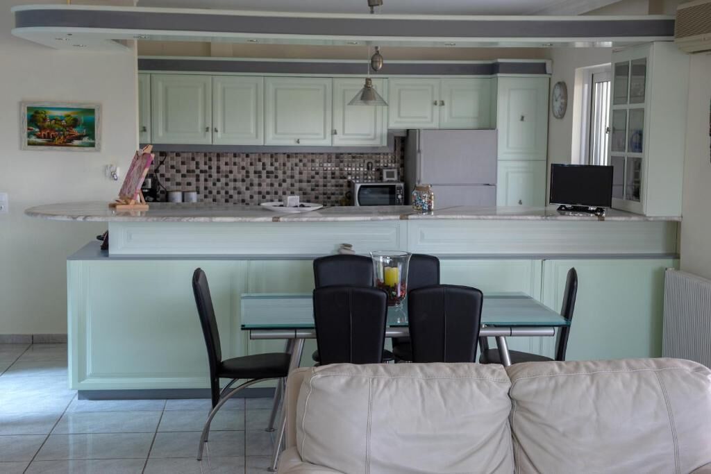 A kitchen with light green cabinets, a glass dining table with four chairs, a microwave, and a refrigerator.