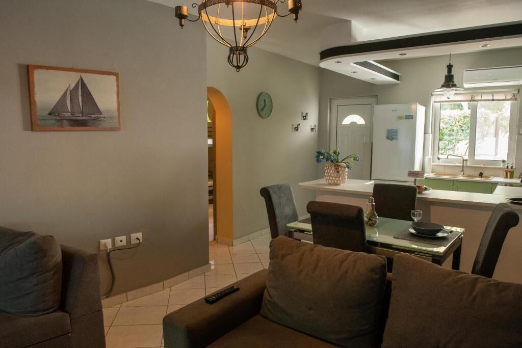 A modern living room with a sofa, a dining area with chairs, a chandelier, and a kitchen area with a window.