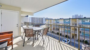 Ein Balkon mit Tisch, Stühlen, einer Tür und Blick auf ein mehrstöckiges Gebäude mit Balkonen.