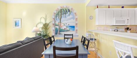 A dining area with a table, chairs, a sofa, and a kitchen area with cabinets and appliances.