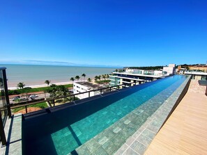 A long, clear swimming pool with a view of the beach and ocean. - Flat FM20 Cabo Branco L3 - By Almare (João Pessoa)