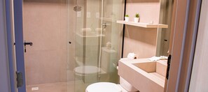 Un baño moderno con ducha de vidrio, inodoro y tocador con espejo y repisa.