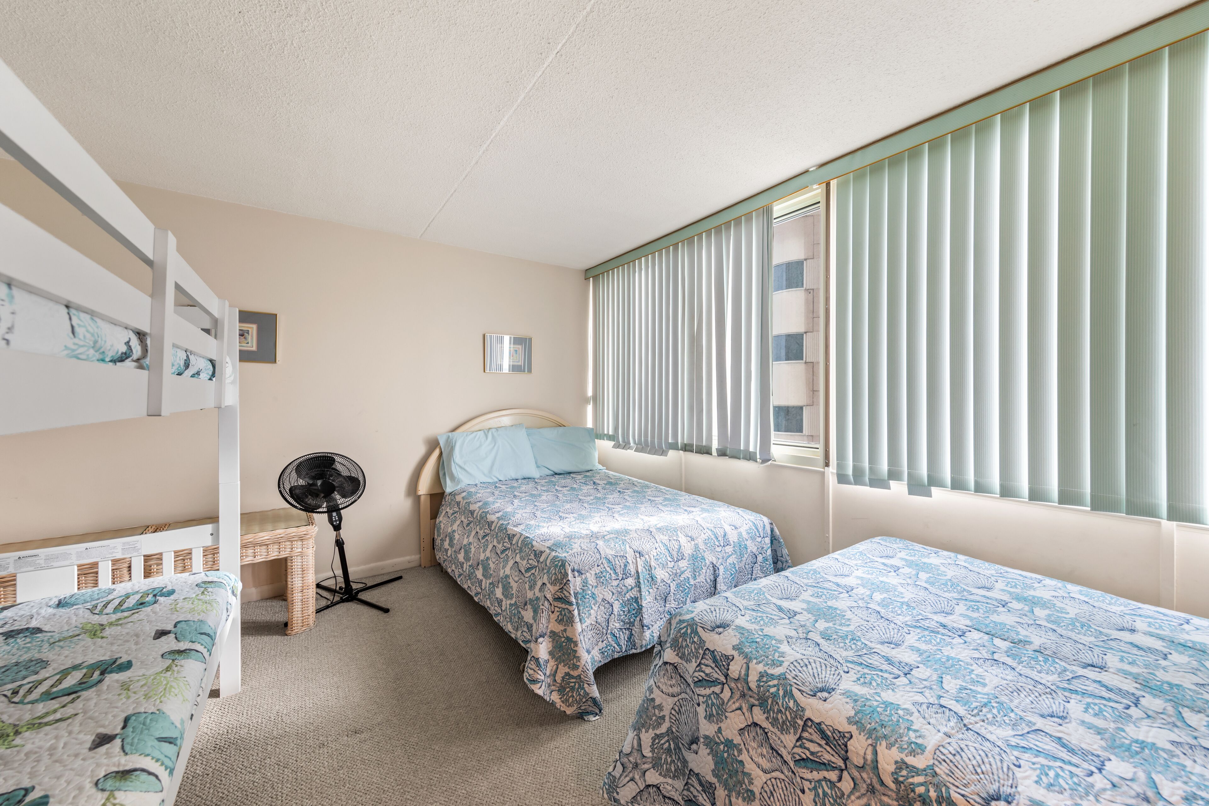 A bedroom with bunk beds, a standing fan, and a window with blinds.