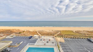Vista a la playa desde un estacionamiento, con piscina y una playa de arena al fondo.