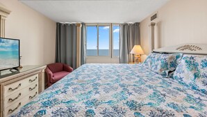 Una habitación de hotel con cama, una silla, televisor y ventana con cortinas.