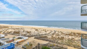 Une vue sur la plage depuis un balcon donnant sur une plage de sable, avec une clôture et un bâtiment au premier plan.