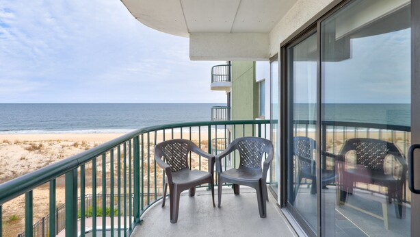 Un balcon avec deux chaises, une porte vitrée et une vue sur la plage et l’océan.