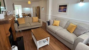 A living room with a wooden coffee table, two sofas with cushions, a white side table, and a framed picture on the wall. - Beach retreat! (Pakefield)
