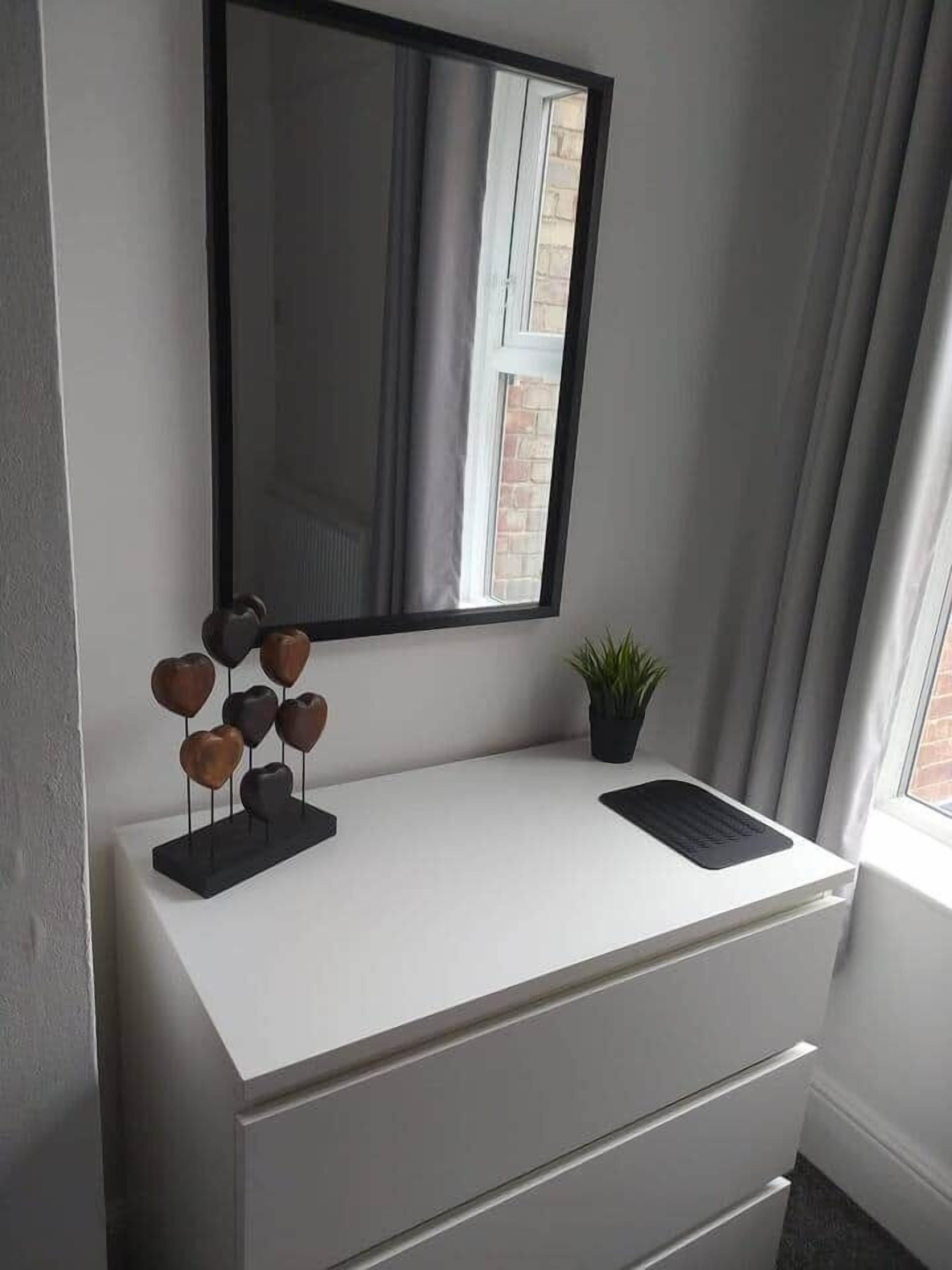 Un bagno moderno con un mobile lavabo bianco, uno specchio e una piccola pianta in vaso.