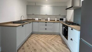 A compact kitchen with grey cabinets, a microwave, a stove, and a sink. - Beach retreat! (Pakefield)