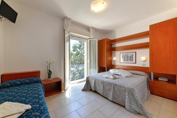 Una habitación de hotel con cama, sofá, armario de madera, mesita de noche con lámpara y ventana con vistas al exterior.