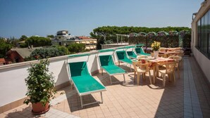A rooftop terrace with sun loungers and a table, overlooking a residential area. - HOTEL TAORMINA (Riccione)