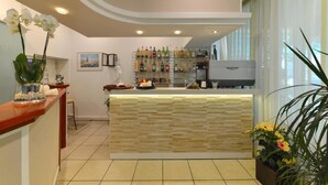 A hotel lobby with a reception desk, a wall-mounted liquor display, and a large window with curtains. - HOTEL TAORMINA (Riccione)