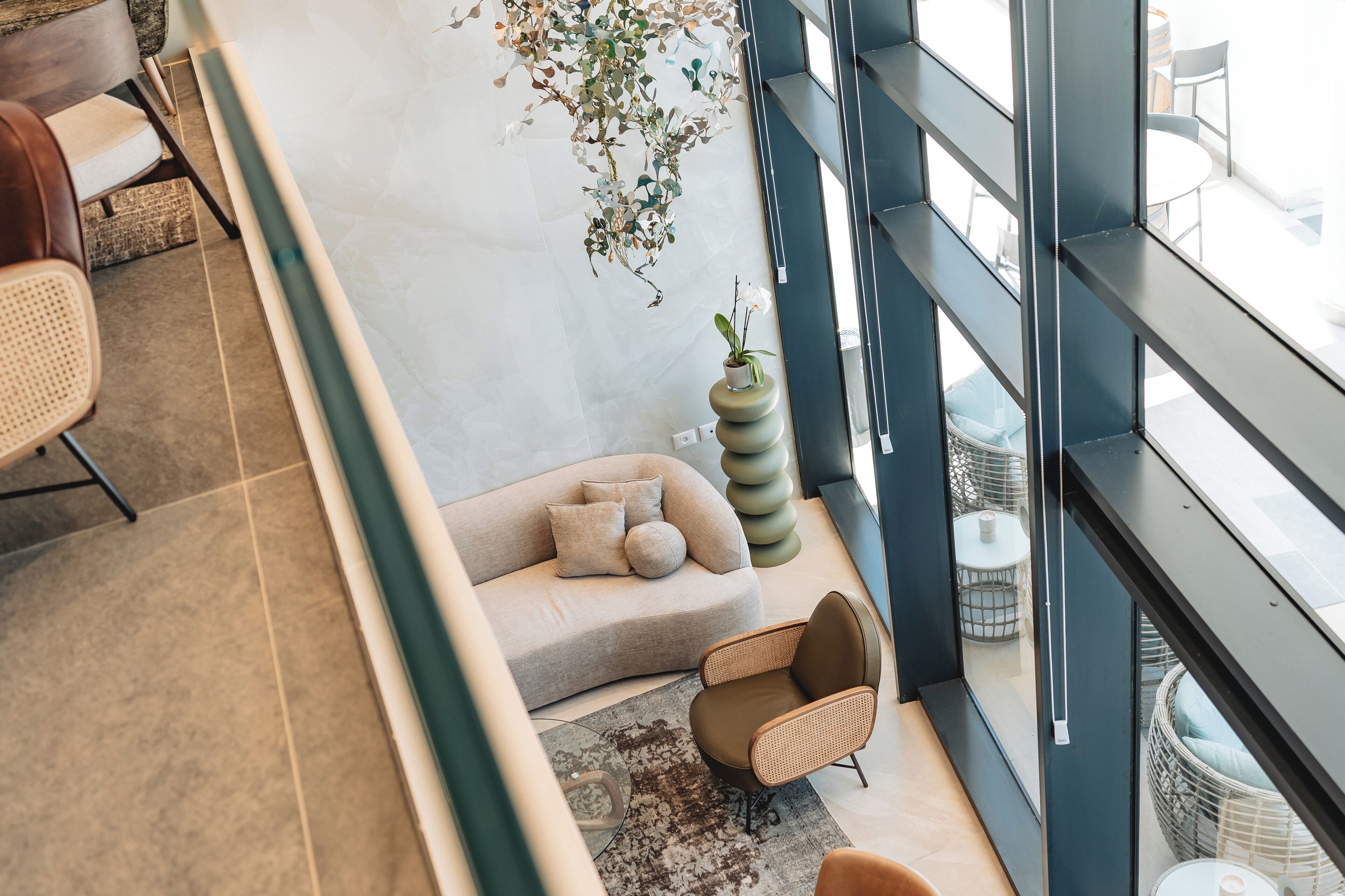 A modern interior with a sofa, chairs, a hanging plant, and a view of the outdoors.