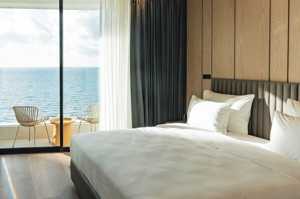 A hotel room with a large bed, a view of the sea, and two chairs by the window. - ALMERA  (Bat Yam)
