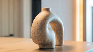 A modern, minimalist vase on a wooden surface in a well-lit room with a neutral color palette.
