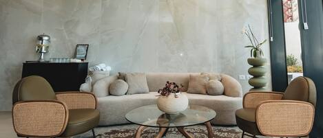 Una sala de estar moderna con un sofá, dos sillas de mimbre, una mesa de centro de vidrio y un jarrón decorativo.