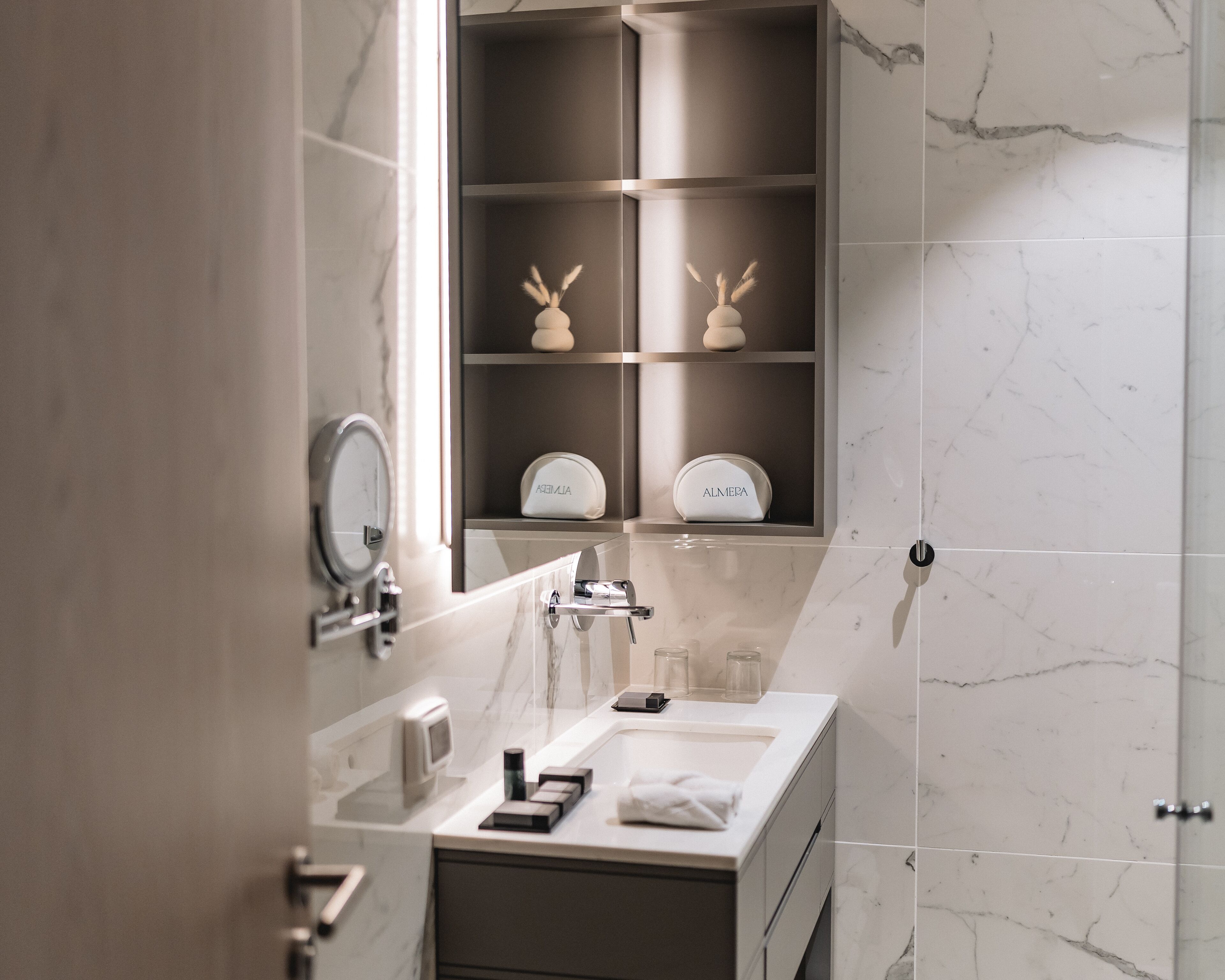 Un baño moderno con tocador de mármol, espejo, toalla y repisa con artículos de aseo.