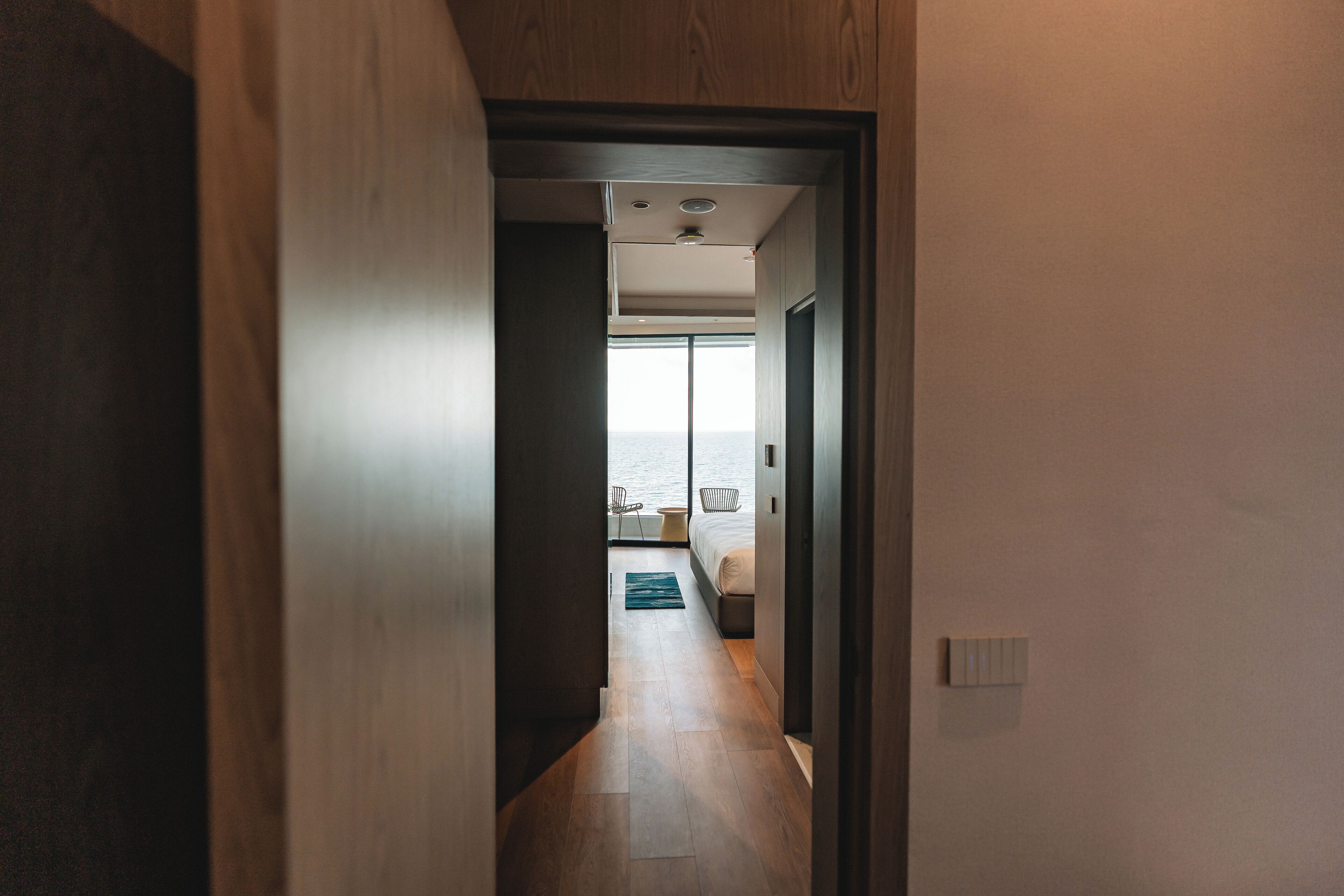 A narrow hallway with wooden flooring leading to a bedroom with a bed and a view of the sea.