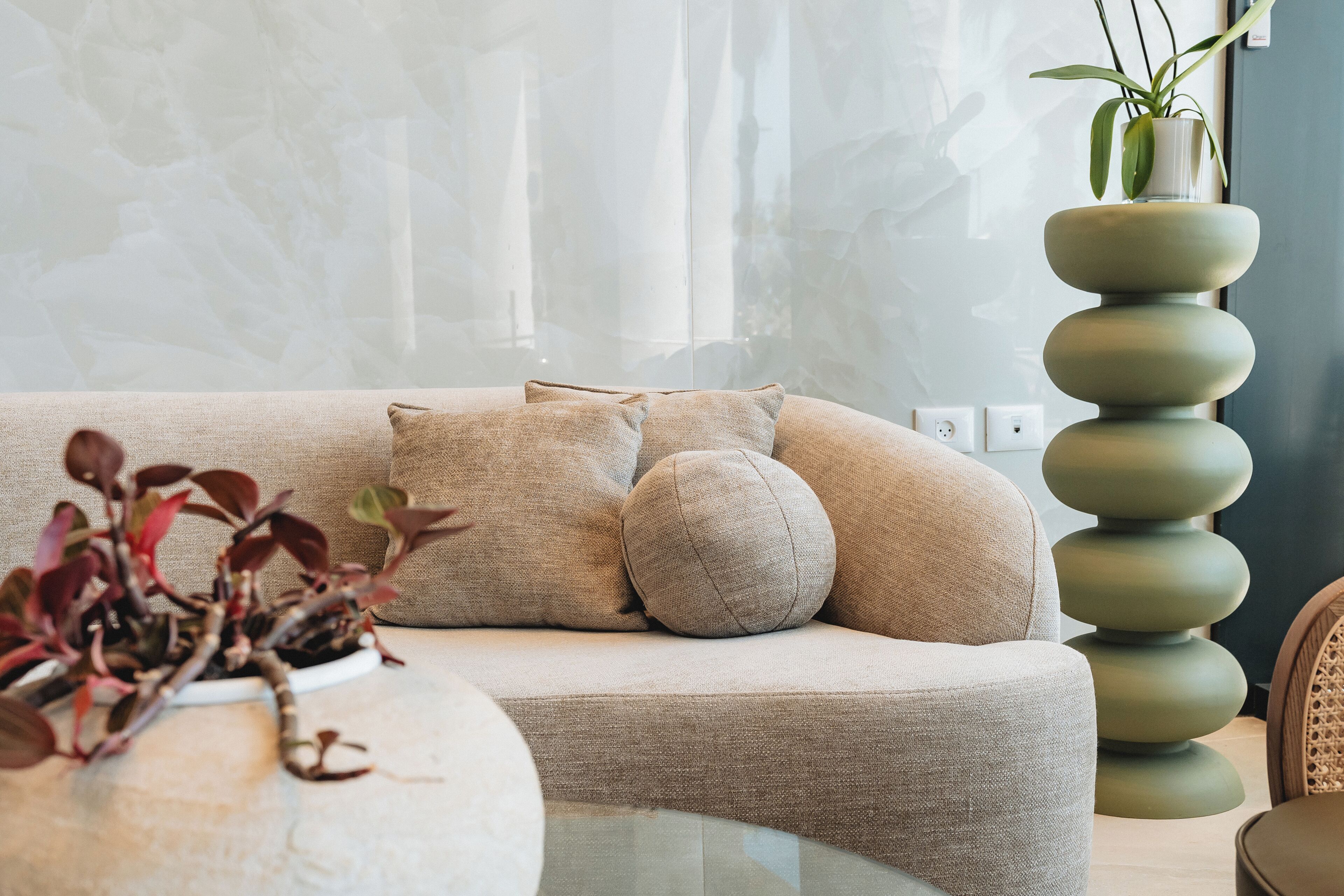 Een moderne woonkamer met een beige bank, een ronde glazen salontafel en een hoge groene plant.