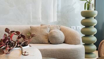 Een moderne woonkamer met een beige bank, een ronde glazen salontafel en een hoge groene plant.