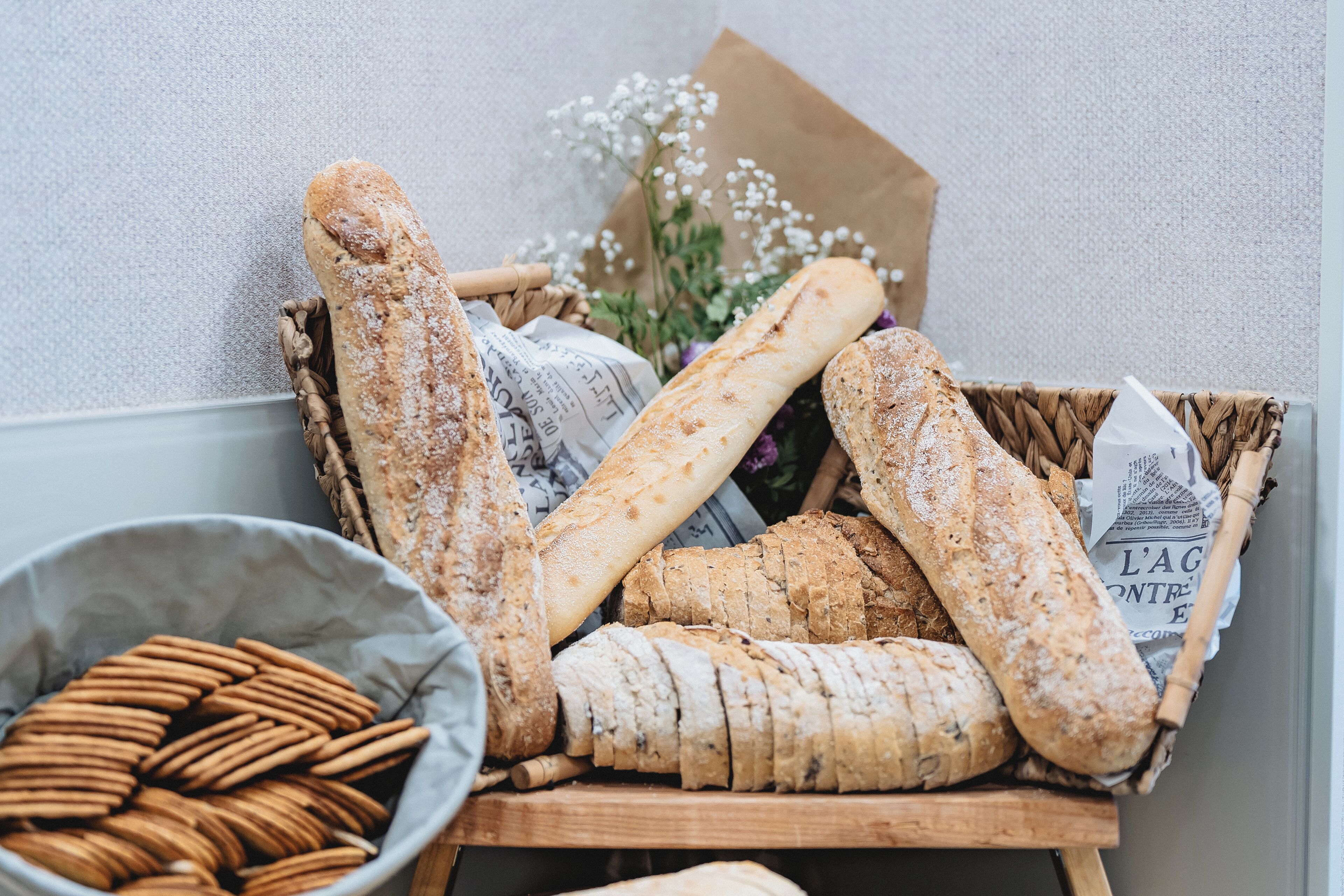 A wooden basket filled with various types of bread and crackers, placed on a table against a textured wall.