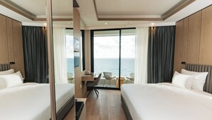 Habitación de hotel con dos camas, un escritorio y vista al mar.
